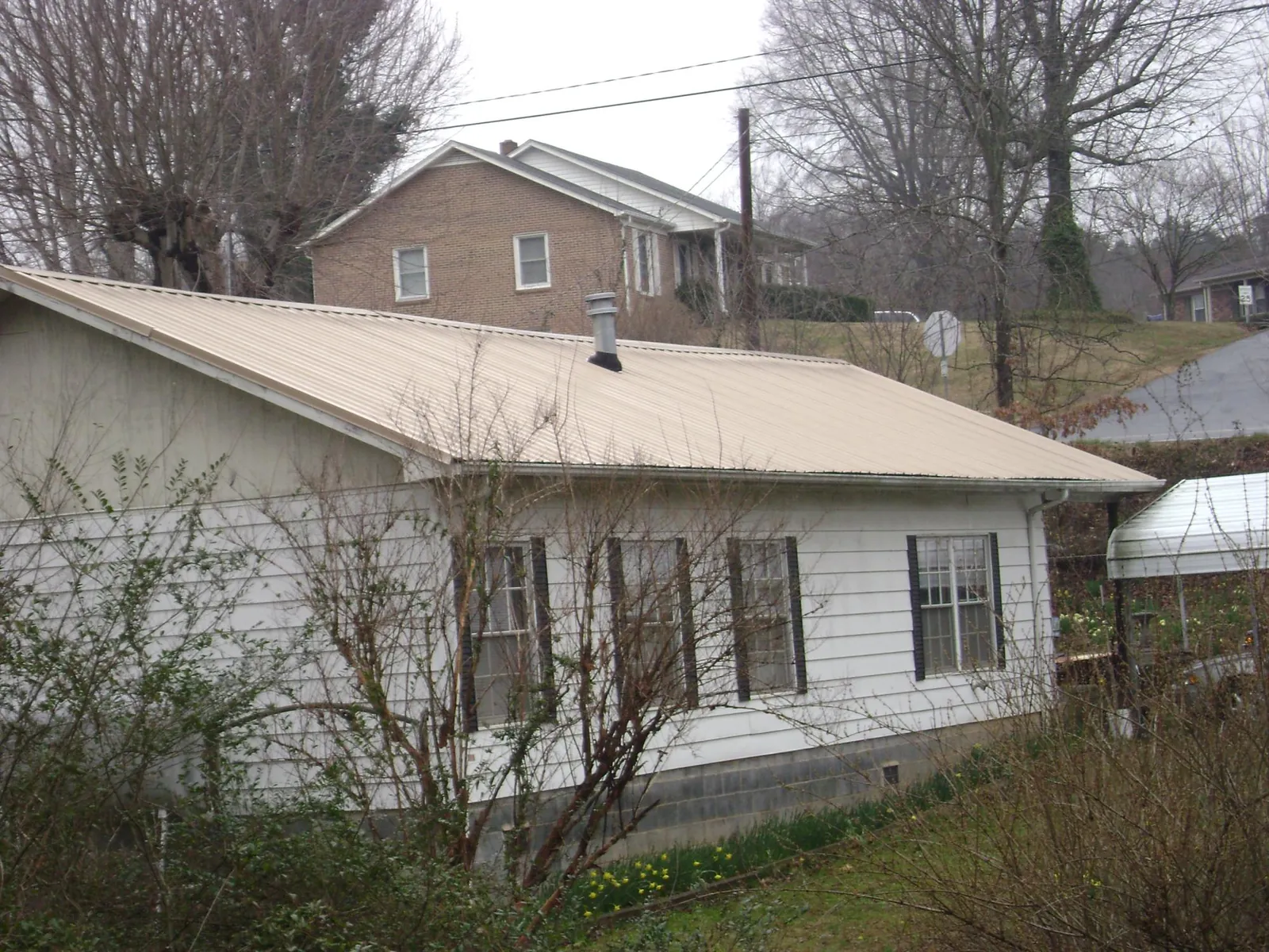 Tan metal roof on a white sided house set into a hillside — Commercial Roofing by Roofing Brothers in Unadilla